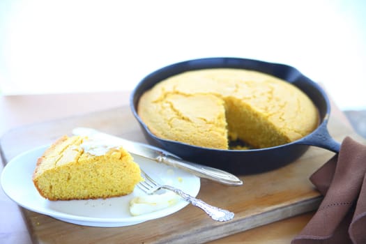 Cornbread baked in a cast iron skillet with a wedge cut with copy space