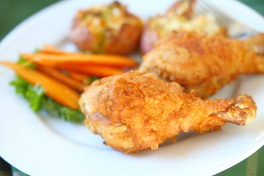 Closeup of fried chicken legs with roasted carrots and crushed potatoes