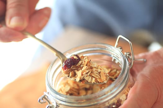 A man removes granola from a jar with a spoon