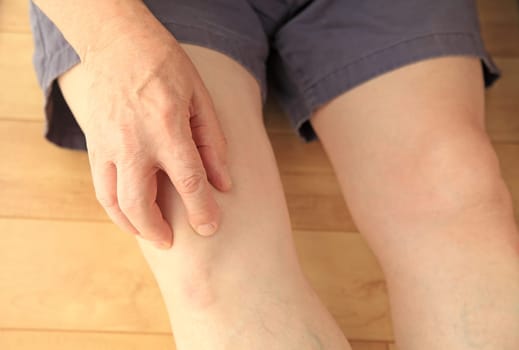 An older man indicates a sore knee while seated on the floor.