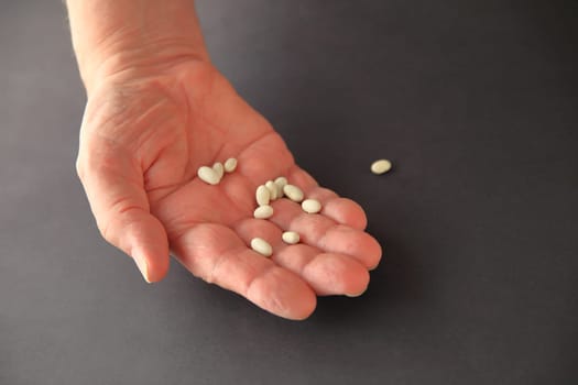 A man holds small white beans in his hand on a dark background