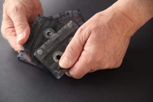 Senior man with three old cassette tapes on a dark background with copy space