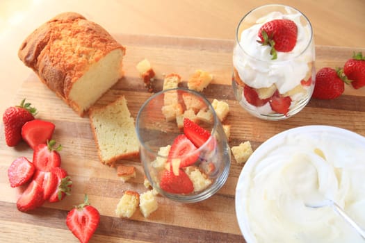 Overhead of strawberries, whipped cream and pound cake with finished miniature trifle on cutting board