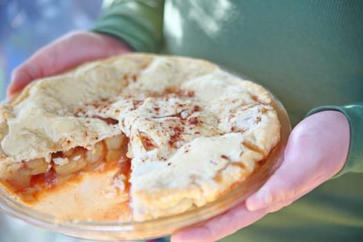 Man holds a freshly-baked apple pie topped with cinnamon on a sunny day.