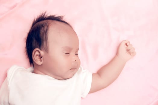 Peaceful baby lying on a bed while sleeping in a bright room over white sheet