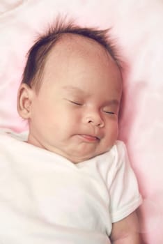 Peaceful baby lying on a bed while sleeping in a bright room over white sheet