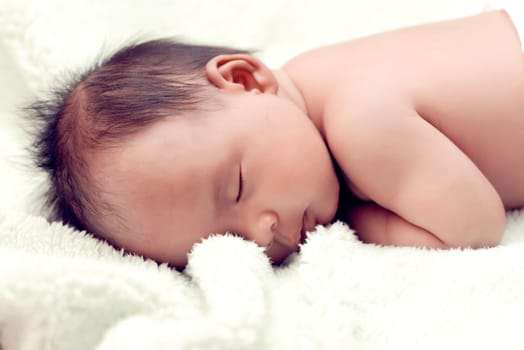 Peaceful baby lying on a bed while sleeping in a bright room over white sheet