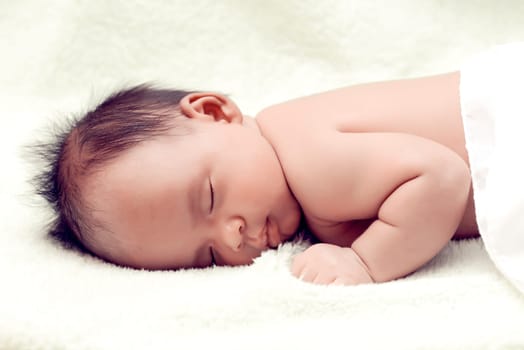 Peaceful baby lying on a bed while sleeping in a bright room over white sheet