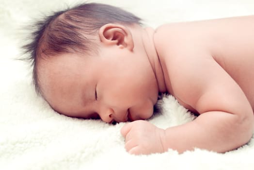 Peaceful baby lying on a bed while sleeping in a bright room over white sheet