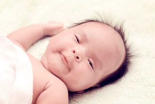 Peaceful baby lying on a bed while sleeping in a bright room over white sheet