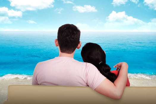 Young couple sitting on the beach looking at the ocean