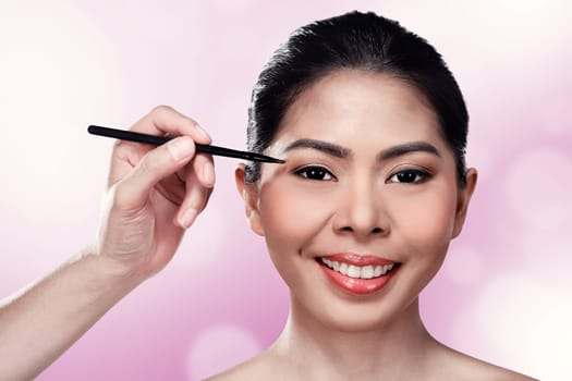 Beautiful asian woman doing makeup over blur background