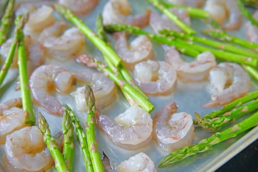 A baking sheet with raw shrimp, asparagus and olive oil