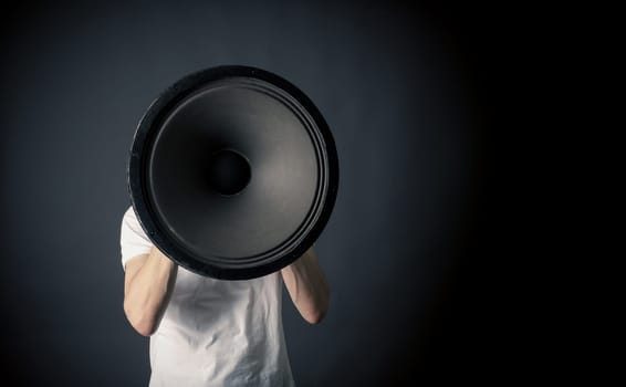 Young man holding a big speaker, speaking loud concept on a dark studio background with space for text or image