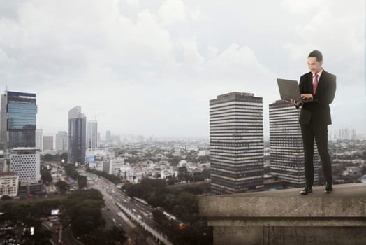 Asian business man typing using laptop on the top of the building