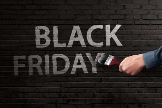 Man hand writing white Black Friday text with brush on the bricks wall