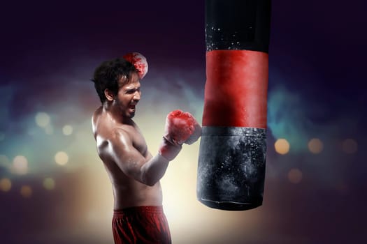 Athletic asian boxer training uppercut with punching bag over blurred light