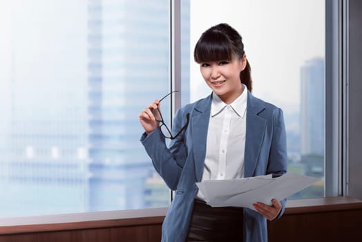 Asian business woman holding paper and glasses over office room background