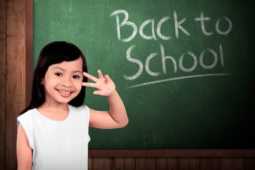 Cheerful smiling little girl on chalkboard background. Looking at camera. Back to school concept