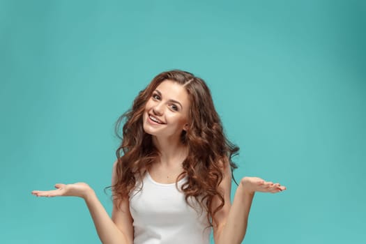 The young woman's portrait with happy emotions on blue background Presenting something