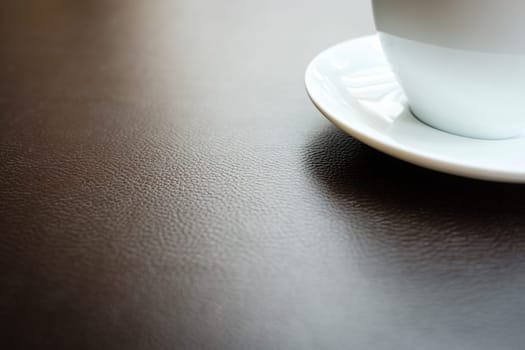 Cup of coffee on brown leather with structure in backlight