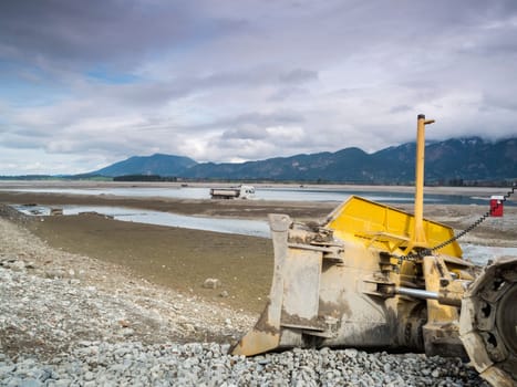 Bulldozer in the drained Forggensee near Füssen / Bavaria. The Forggensee is fed by thawing snow from the high Alps and is a reservoir for sedimentary rocks. In spring,the lake is emptied to remove the sedimentary rock. In summer,the lake has returned to its normal water level and is navigated by excursion boats.