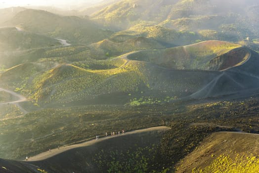 Group of tourists walking on the edge of the crater. Fog at sunset over the volcano Etna