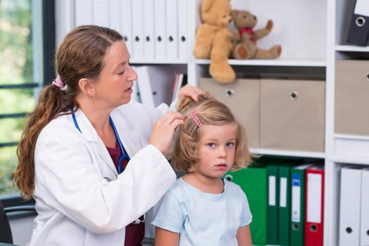 female pediatrician in white lab coat examined little girl for lice