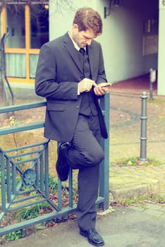 businessman in suit in front of city- background with smartphone