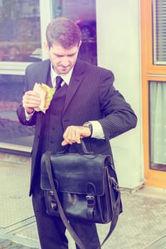 businessman in suit in front of city- background is eating and looking for time