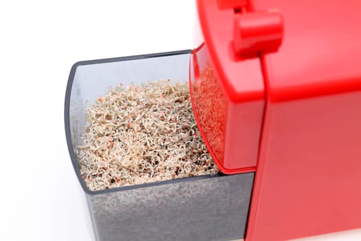 Red pencil sharpener with pencil trash on white background
