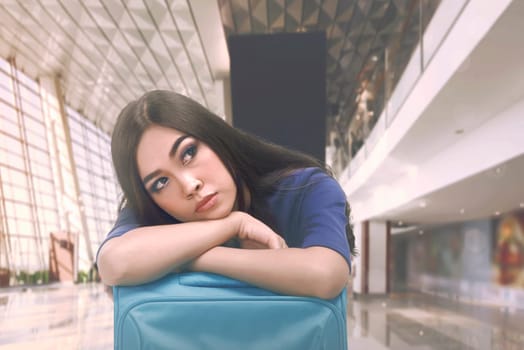 Beautiful asian tourist with sleepy expression on suitcase at airport terminal