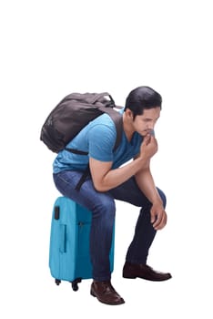 Portrait of asian tourist sitting on suitcase thinking isolated over white background