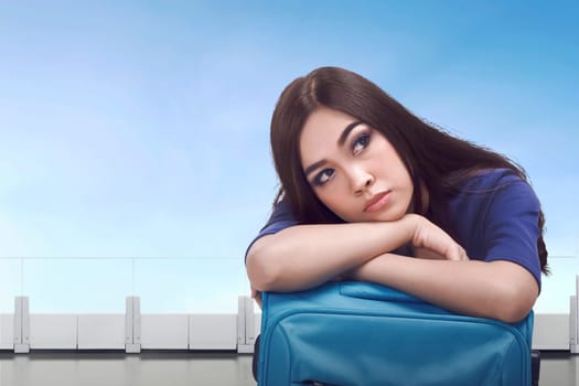Bored asian tourist woman waiting with luggage at airport terminal