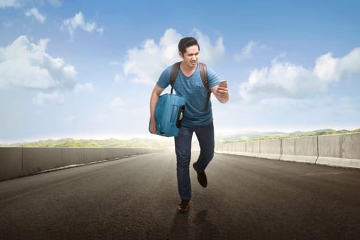 Young asian tourist running with holding phone and suitcase on the road