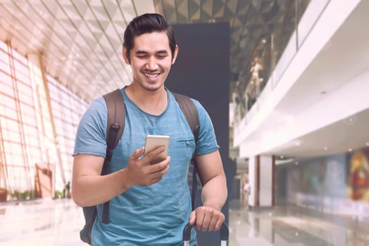Happy asian tourist holding phone and suitcase in the airport
