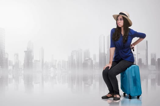 Young asian woman with unhappy face sitting on a suitcase over abstract background