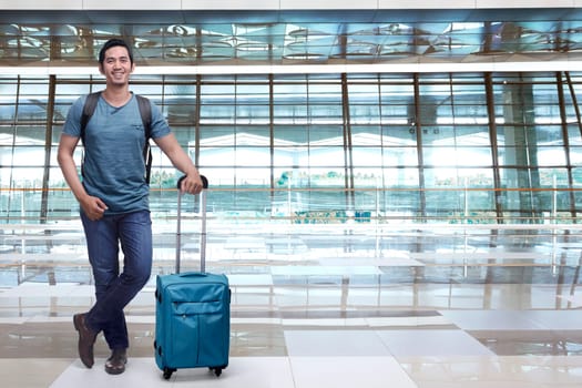 Handsome asian man backpacker holding blue suitcase in the airport terminal