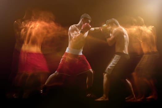 The two male athlete boxers punching with dramatic edgy lighting in a dark studio. Image made with stroboscope