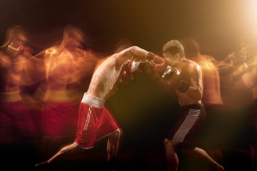The two male athlete boxers punching with dramatic edgy lighting in a dark studio. Image made with stroboscope