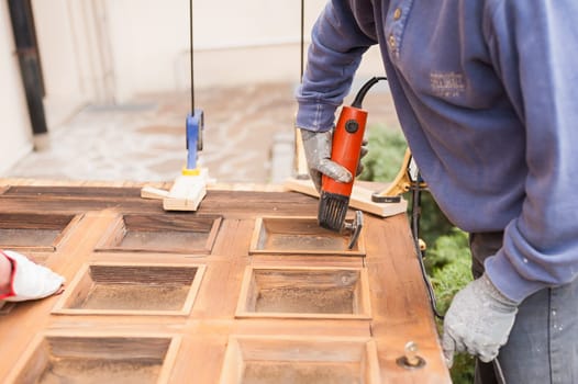 Carpenter at work with angular Sander. Maintenance and restoration of an old wooden door.