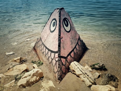 A big stone with graffiti standing on the beach shore near the water