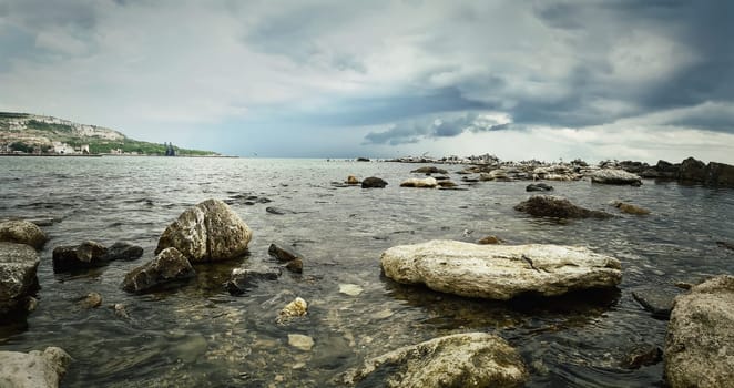 Seascape of stone beach with a dramatic cloudy sky. Beautiful view at the coast of the Black Sea in Balchik city, Bulgaria.