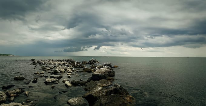 Seascape of stone beach with a dramatic cloudy sky. Beautiful view at the coast of the Black Sea in Balchik city, Bulgaria.