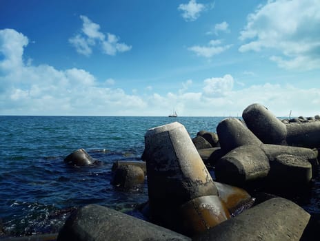 Huge stones in the sea water near the harbor at Balchik city, Bulgaria. Summer vacation background with a ship floating on far.