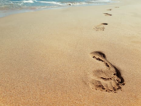 Closeup of footprints in sand at the beach near the water. Journey concept