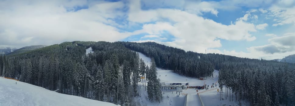 Winter sunshine panorama in the forest. Lovely winter landscape with the evergreen fir forests warmed up by the sun and its rays while everything is covered in snow. Bukovel, Ukraine.