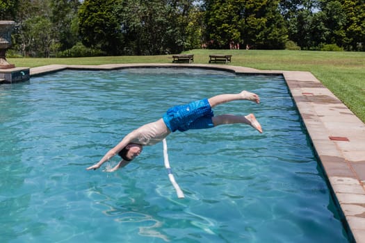 Boy running jumping diving into home  swimming pool summer playtime