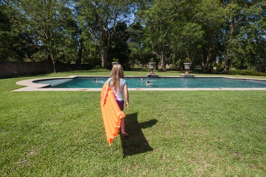 Young girl walking to swimming pool with orange air matt summertime at home.