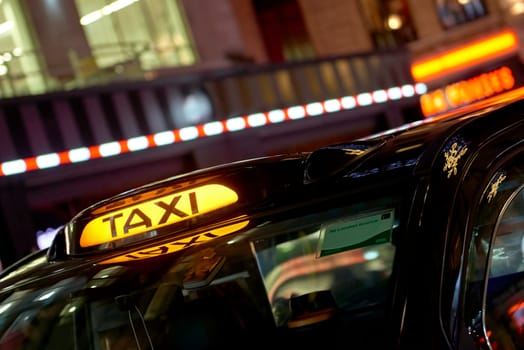 Low key detail of London black cab sign turned on at night, with shop lights in the background.